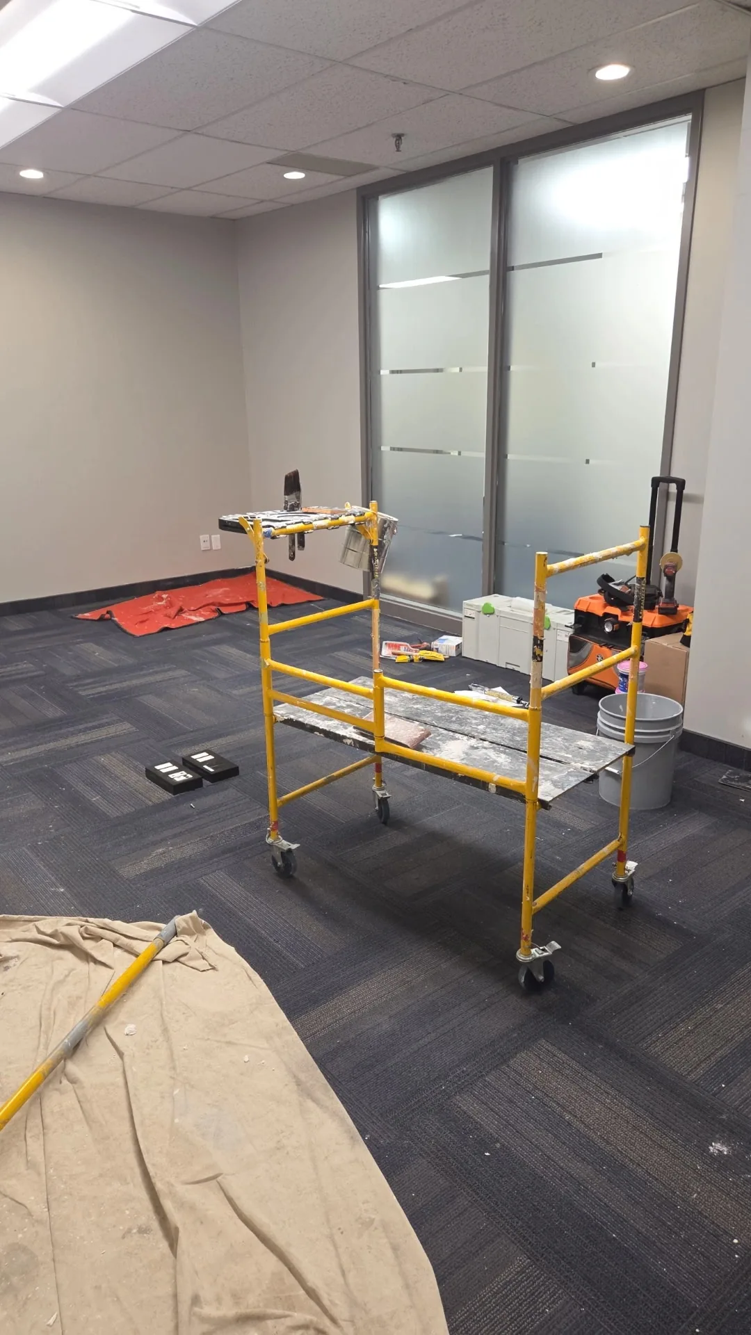 Office walls and a glazed partition with painting equipment and protected floor areas