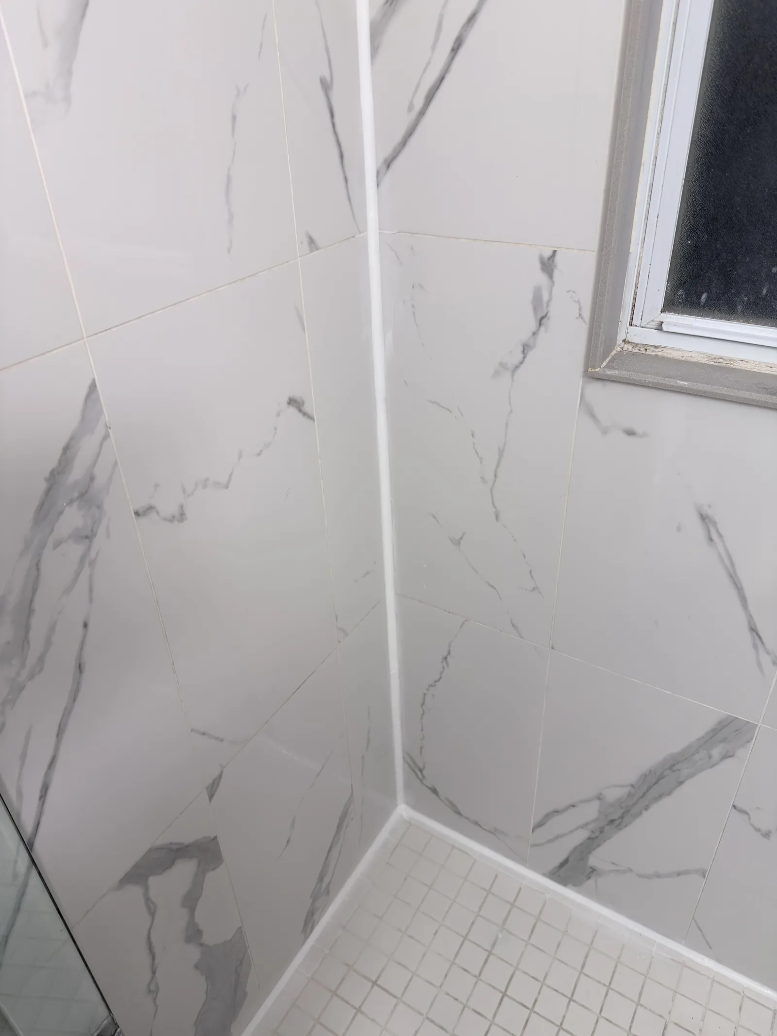 White sealant along the corner and floor joints of a tiled shower